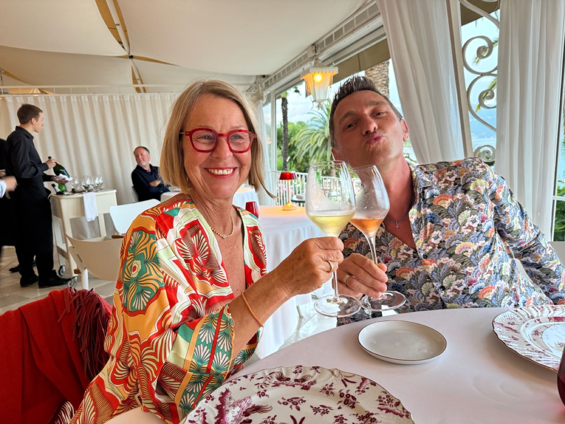 Chris stößt in einem hellen Restaurant am See mit einer Teilnehmerin an