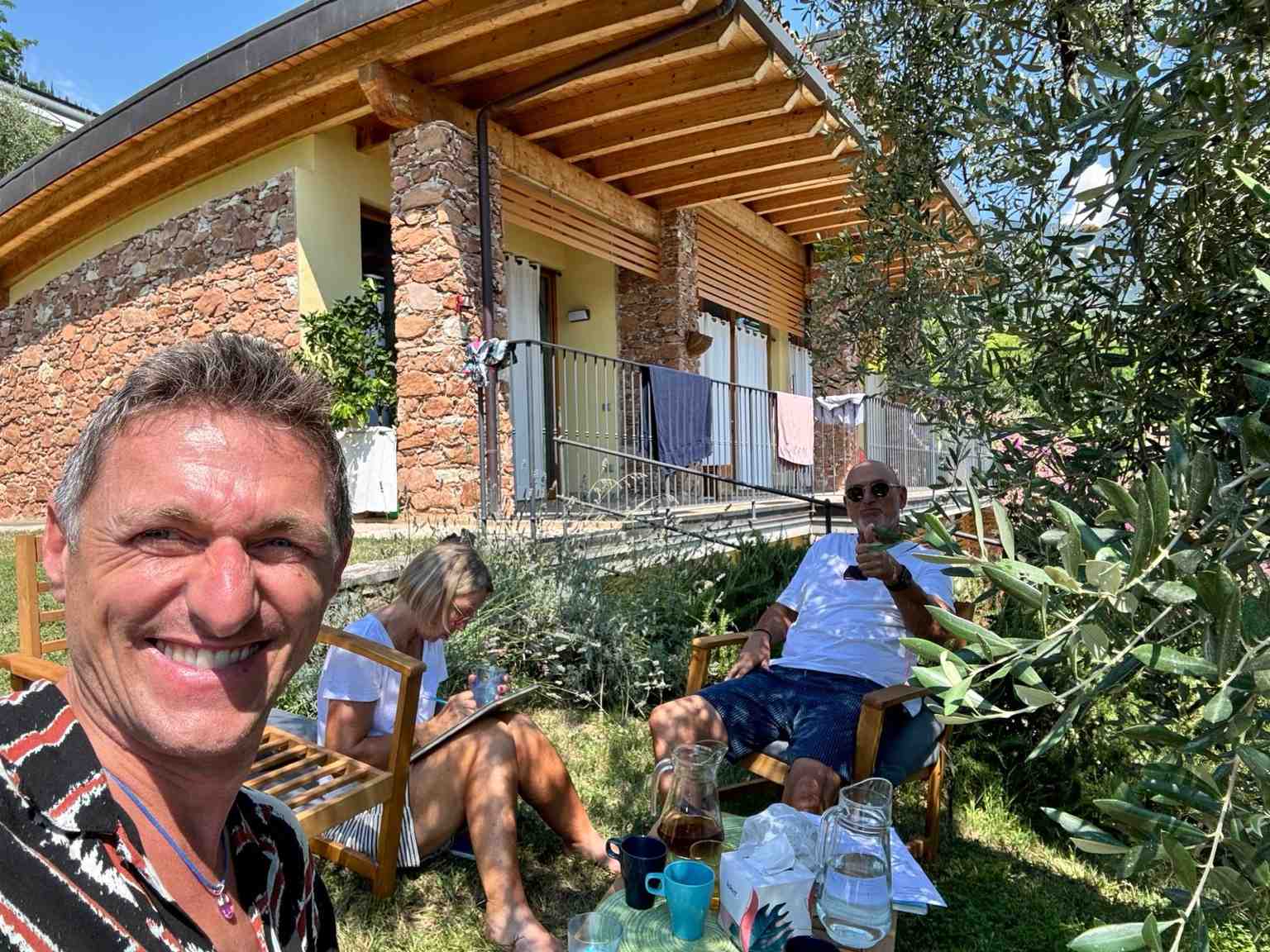 Chris Spieler mit zwei Teilnehmenden in einem sonnigen Garten, umgeben von Olivenbäumen und Natur – ein Moment der Ruhe, Achtsamkeit und Verbundenheit während eines Personal Retreats.